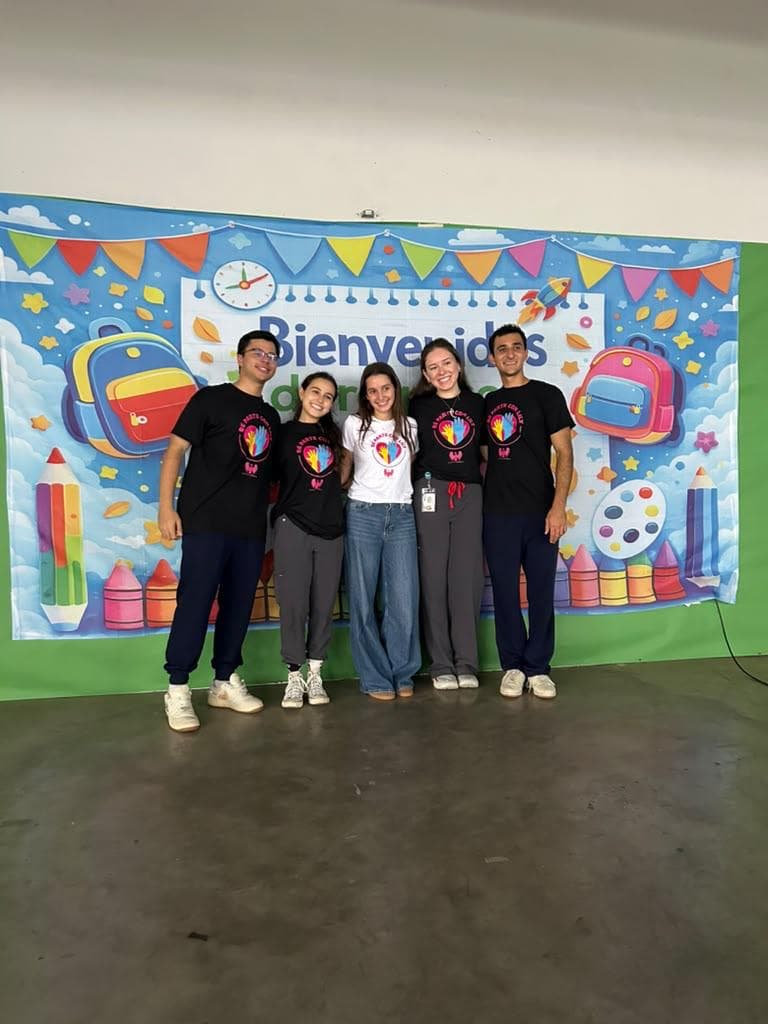 Cinco miembros de la comunidad sonríen frente a una decoración de bienvenida